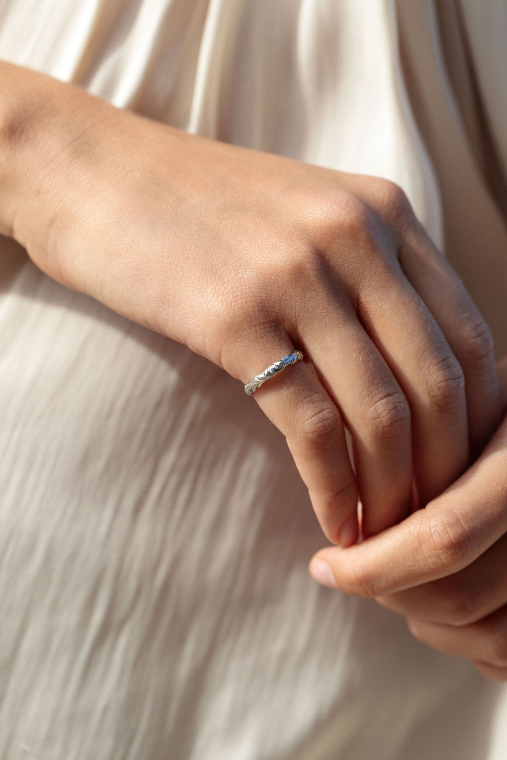 Hand resting on cream fabric wearing a slim 3mm gold Hawaiian wave edge ring