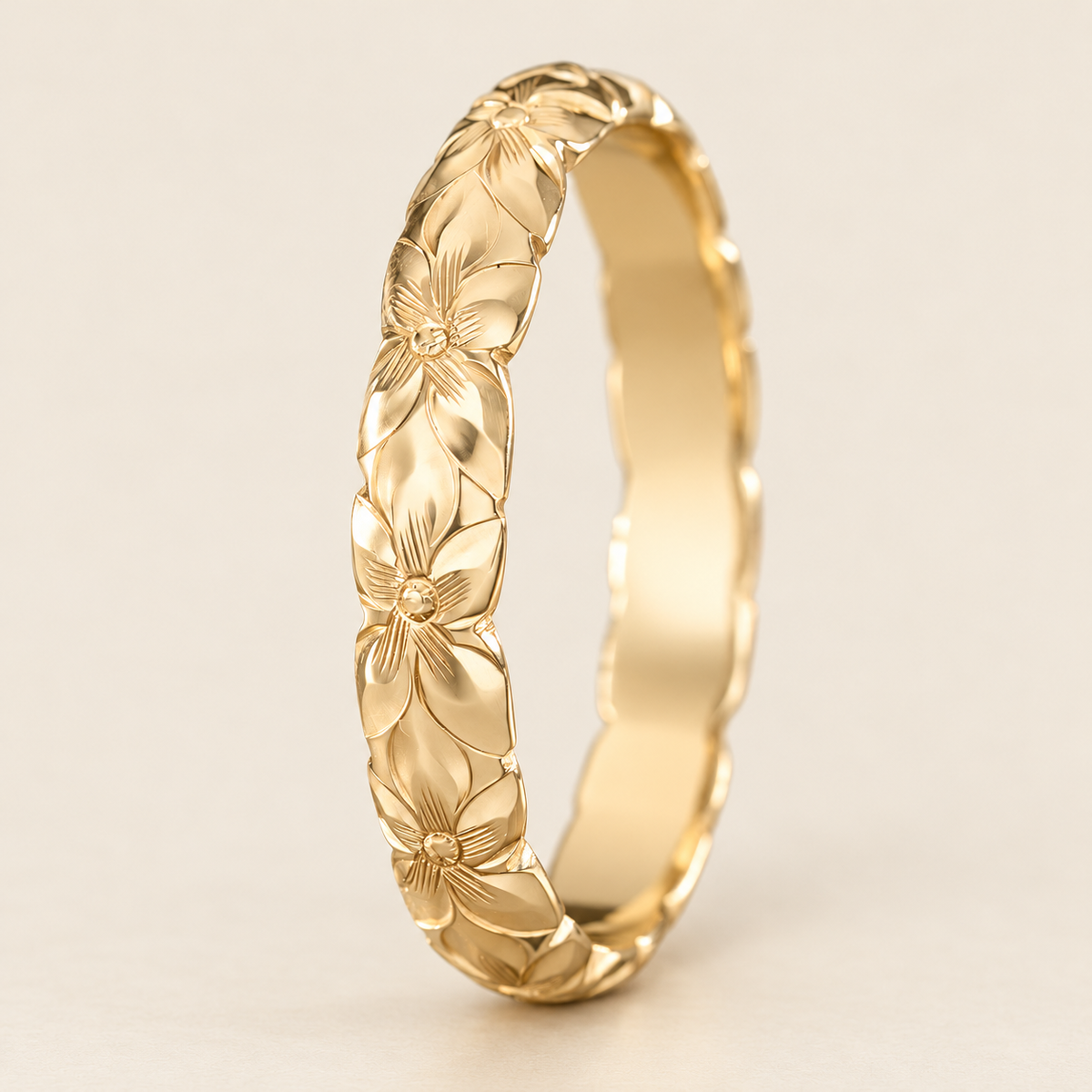 Yellow gold 4mm ring with hand-engraved plumeria flowers and scalloped edges, standing upright on an ivory background.