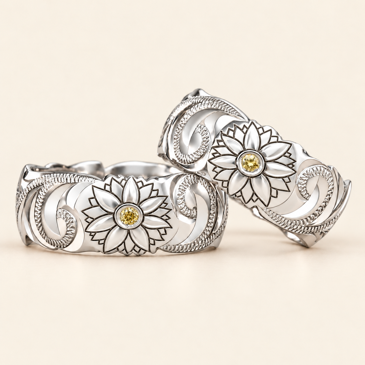 Two white gold Hawaiian sunflower rings with round yellow center stones and engraved scrollwork, shown on ivory.