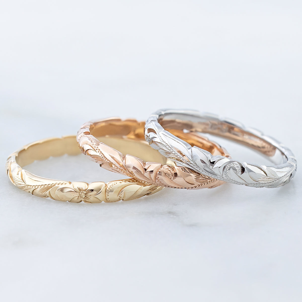 Three 3mm Hawaiian wave edge bands in yellow, rose and white gold on a marble surface