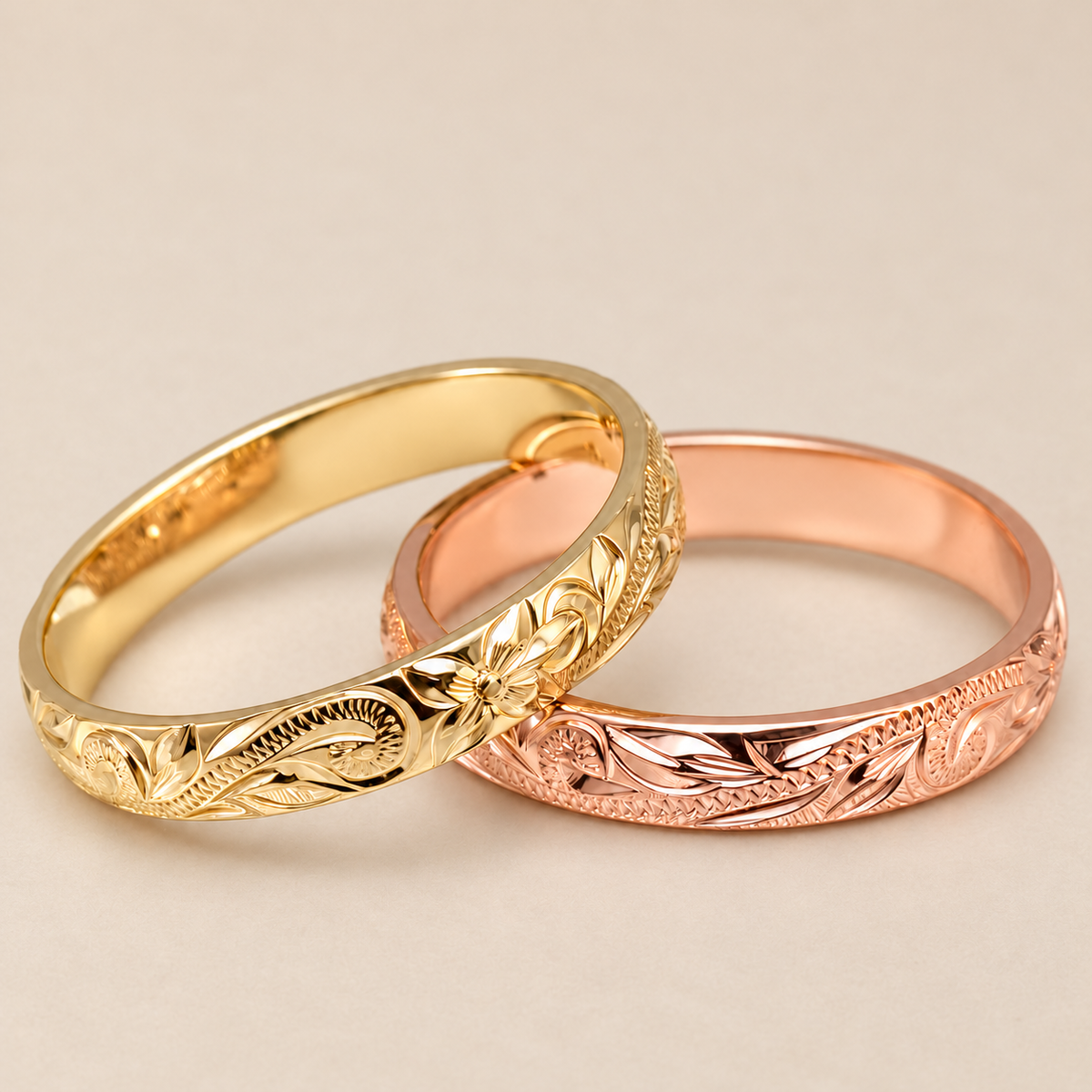 Yellow and rose gold 3mm Hawaiian heirloom barrel rings with hand-engraved plumeria and scroll designs on an ivory background