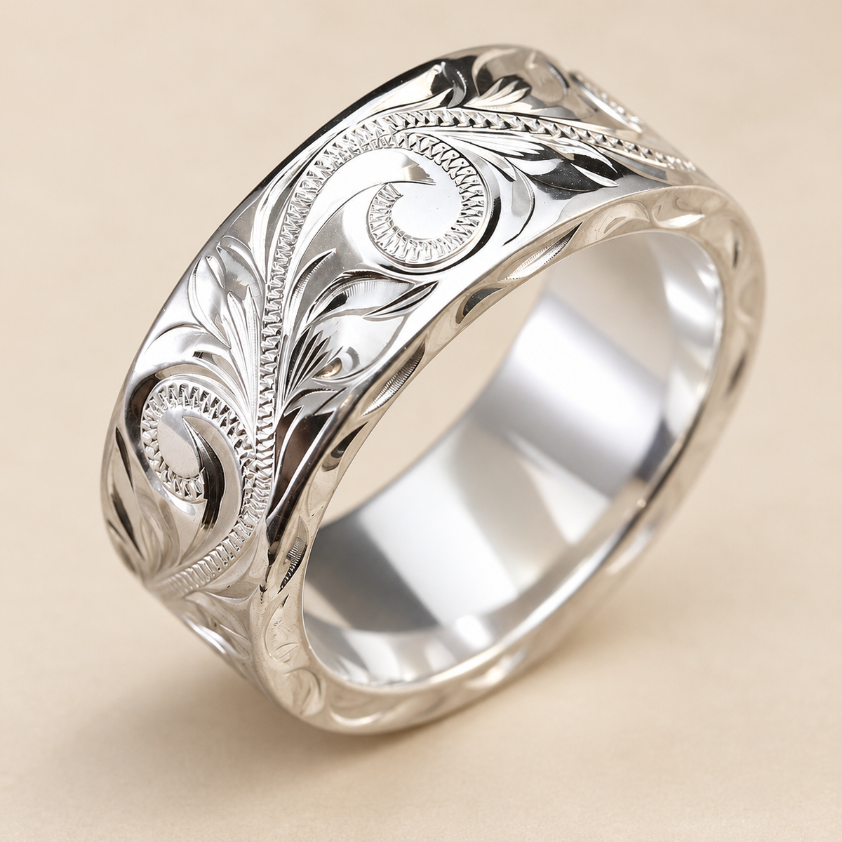 8mm wide, 2mm thick sterling silver Hawaiian hand-engraved flat ring with scroll and leaf details, angled view on an ivory background
