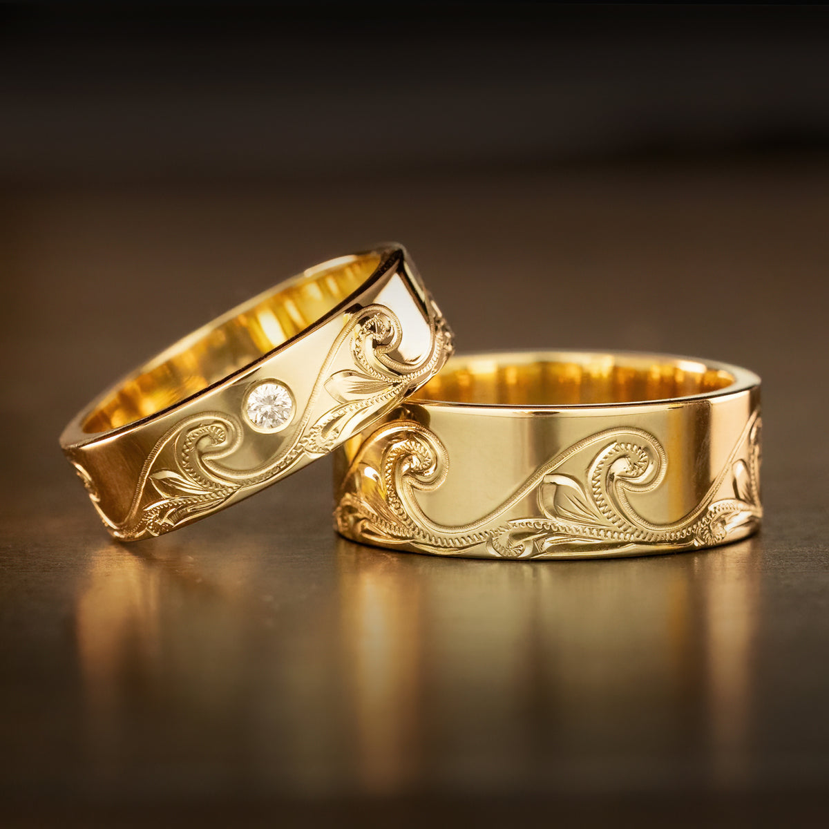 Pair of 14K gold Catch the Wave rings with bezel set diamonds on a dark background