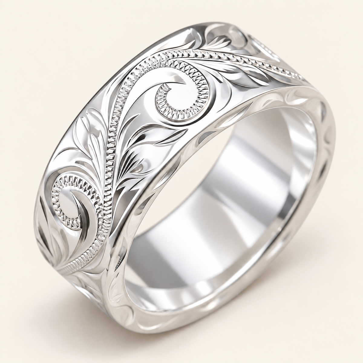 Heavy 8mm wide, 2mm thick sterling silver Hawaiian ring with hand-engraved scroll and leaf design, angled view on ivory.
