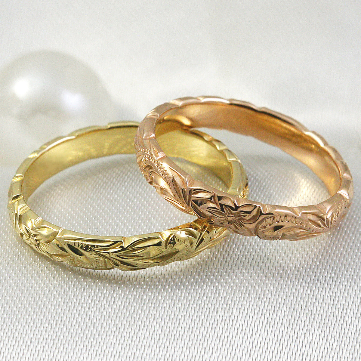 Yellow and rose gold 3mm hand engraved wave edge bands resting against pearls