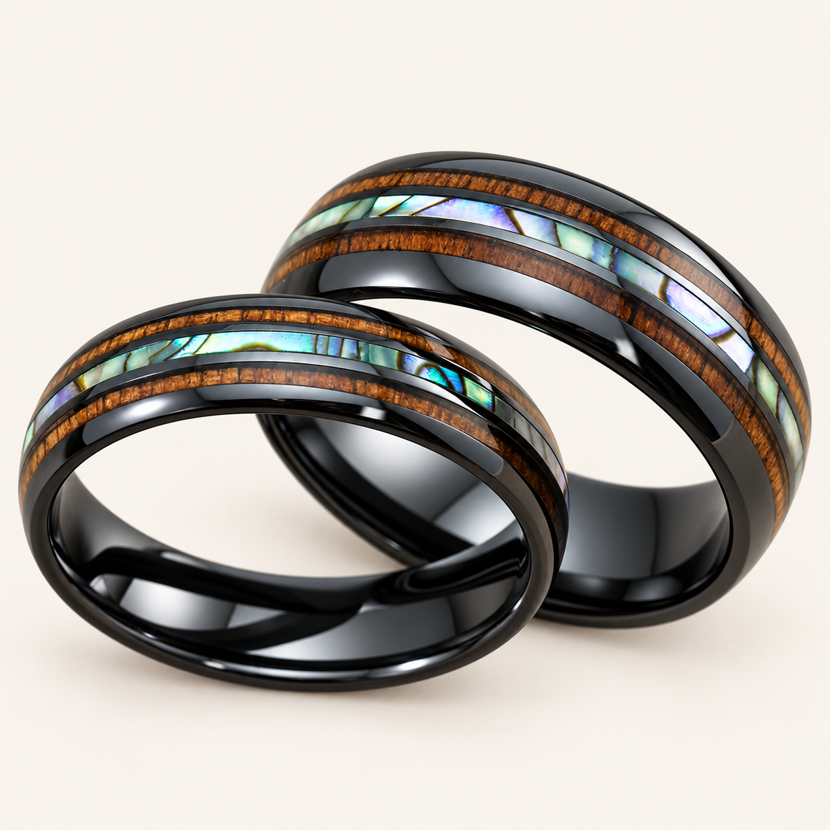 Pair of 6mm and 8mm black ceramic rings with central abalone shell and Hawaiian koa wood inlays, on an ivory background
