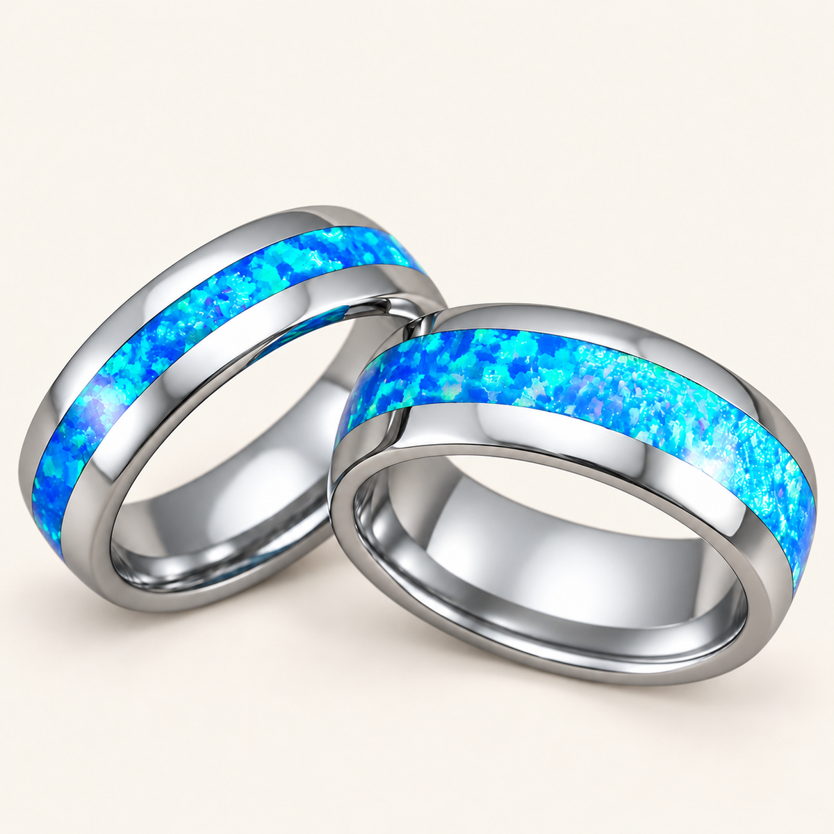Pair of polished tungsten carbide wedding bands with central blue opal inlays, 6mm and 8mm, on ivory