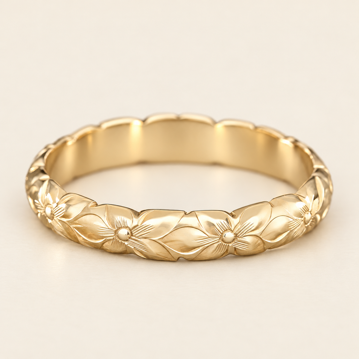 Yellow gold 4mm ring with hand-engraved plumeria flowers and scalloped edges, shown in a low side view on ivory.