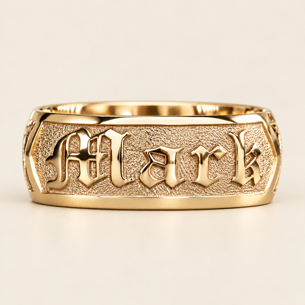 Yellow gold personalized name ring with raised Old English Mark lettering on a textured panel, front view on ivory