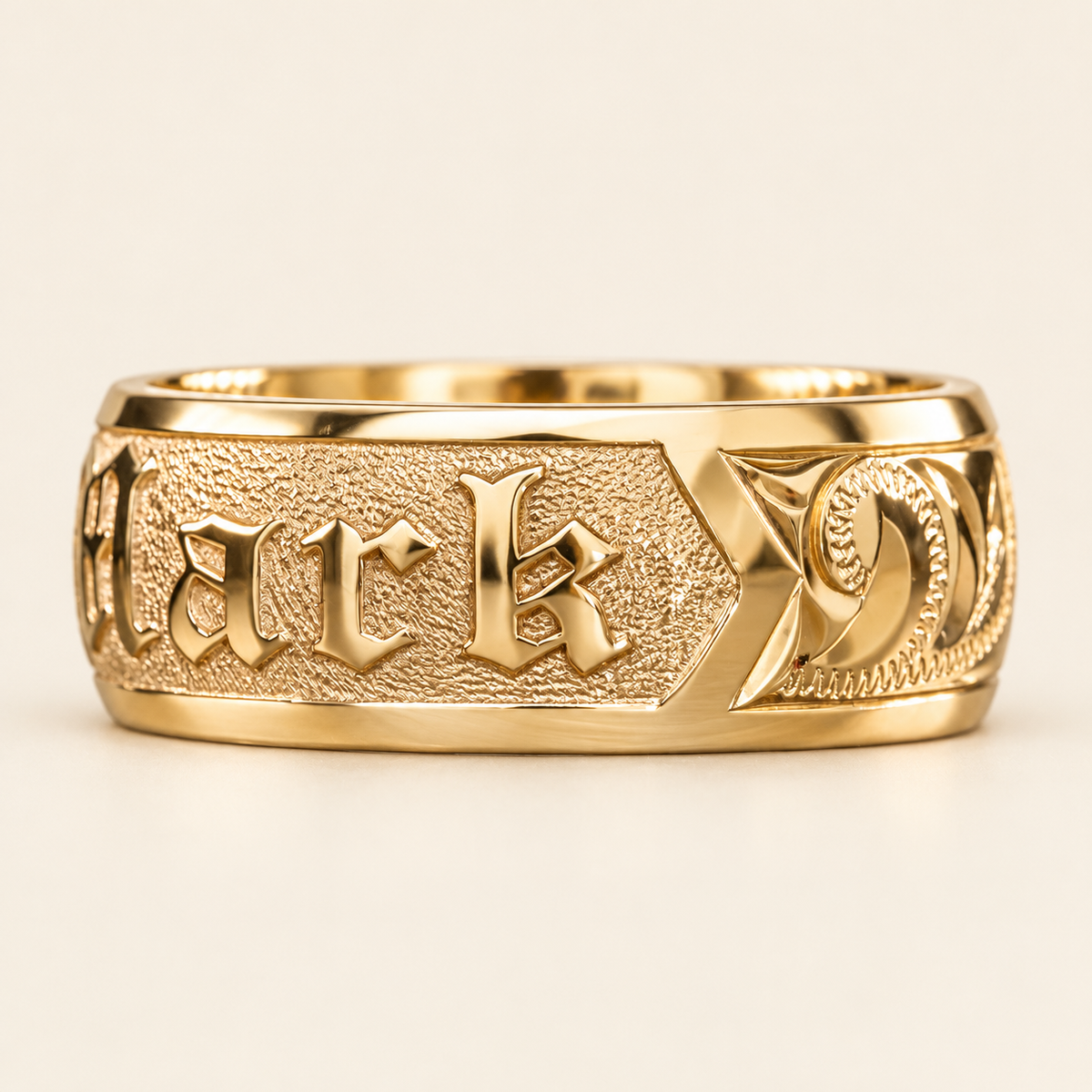 Yellow gold personalized name ring with partial Old English lettering and hand engraved scroll shoulder, angled view on ivory