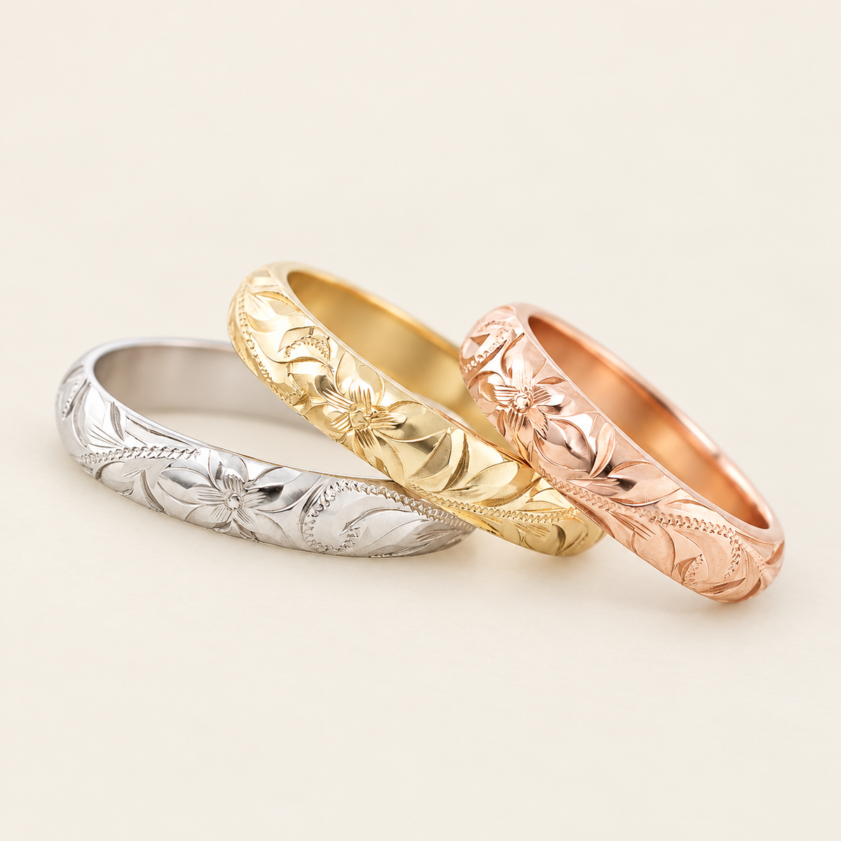 Three 4mm Hawaiian Heritage rings in white, yellow and rose gold, angled view on an ivory background