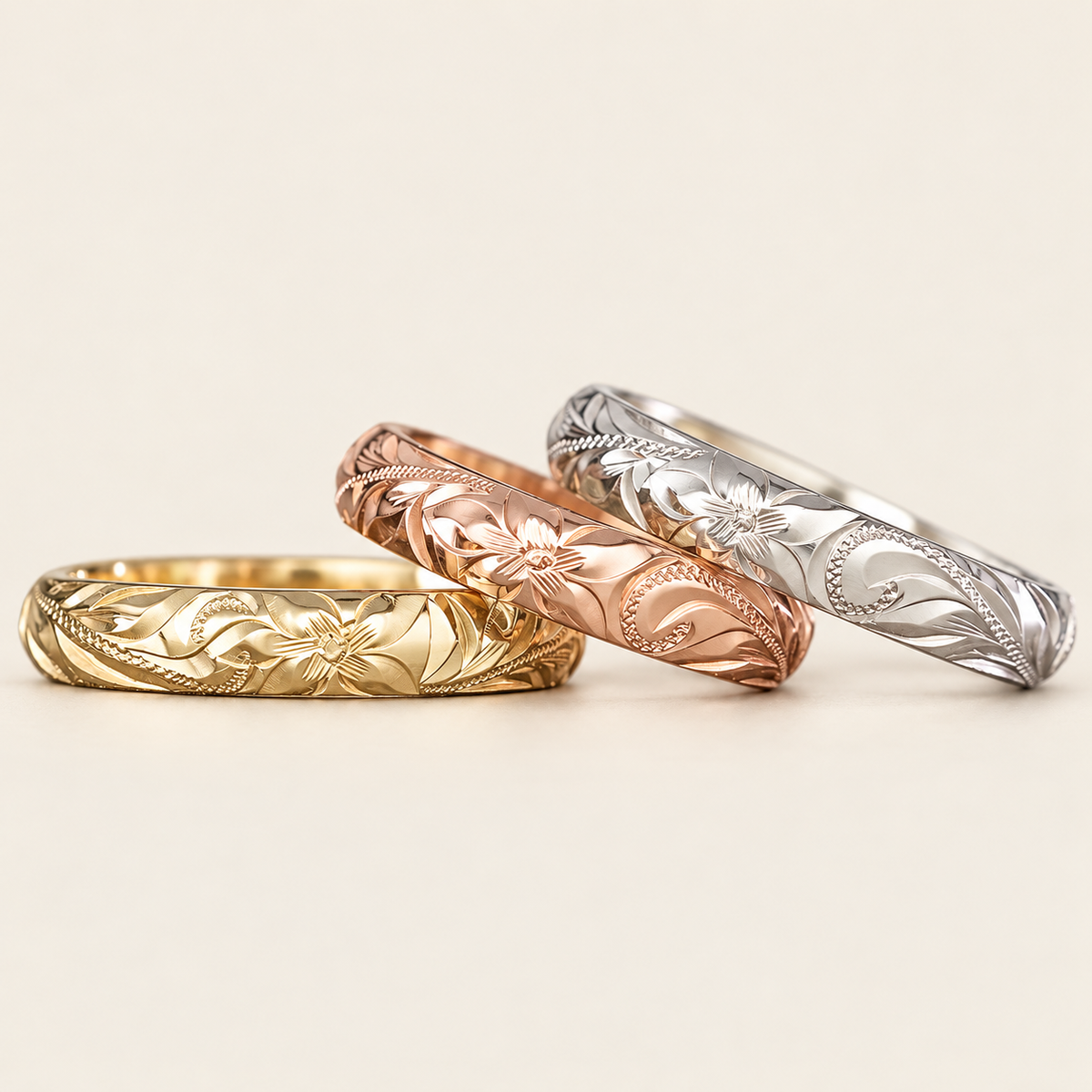 Three 4mm Hawaiian Heritage rings in yellow, rose and white gold, low front view on an ivory background