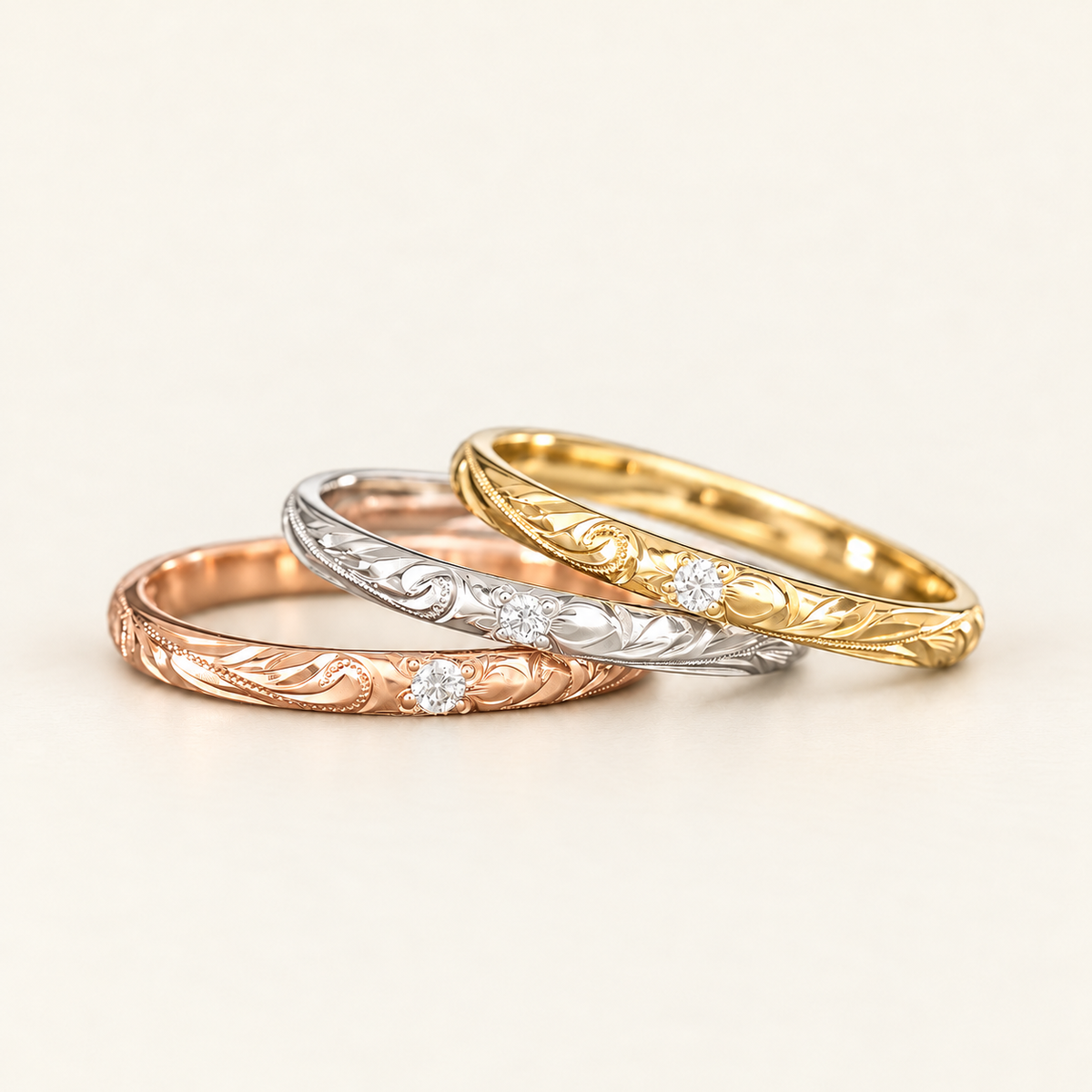 Rose, white and yellow gold Hawaiian rings with round clear stones and hand-engraved scrolls and leaves on ivory.