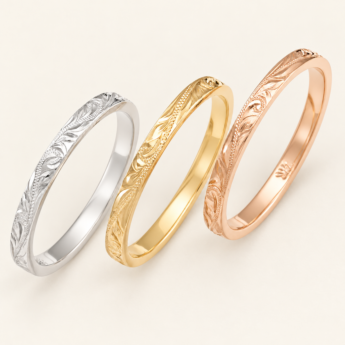 White, yellow and rose gold 2mm Hawaiian rings with flat profiles and hand-engraved leaves and scrolls, shown on ivory.