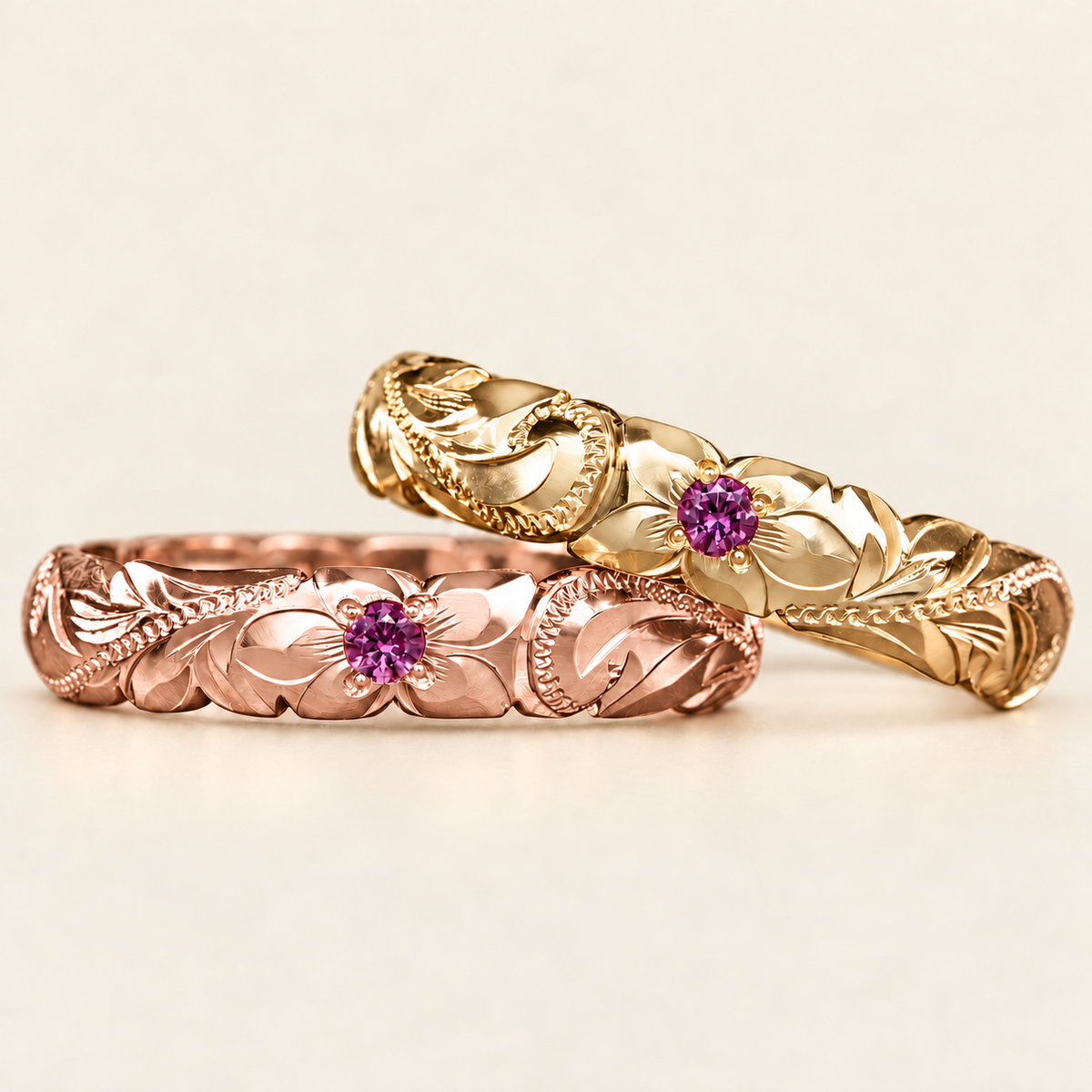 Rose and yellow gold Hawaiian rings with pink sapphires, floral and scroll engraving, on an ivory background.