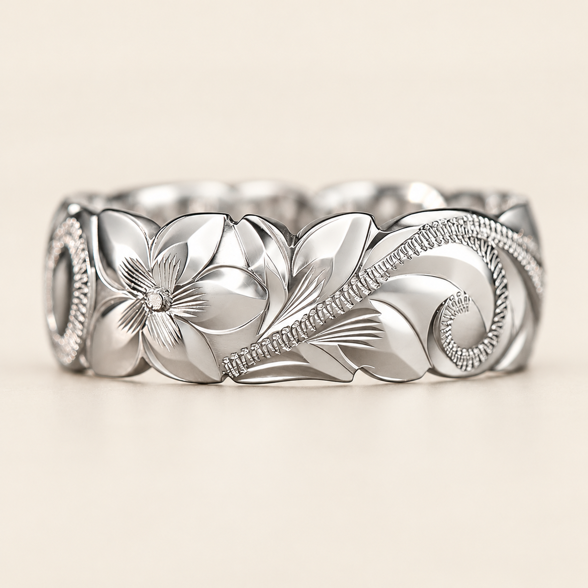 Front view of a white gold 8mm Hawaiian ring with wave edges and hand-engraved flower, leaves and scrollwork, shown on ivory.