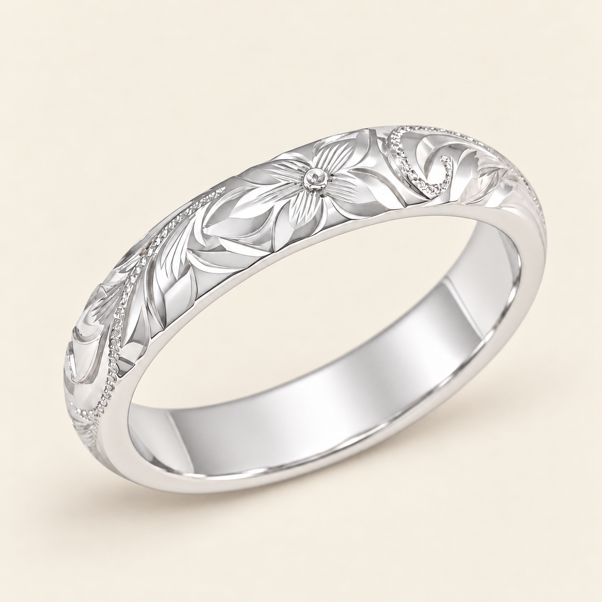 White metal Hawaiian ring with a heavy rounded 4mm profile and hand-engraved plumeria, leaves and scrollwork, shown on ivory.