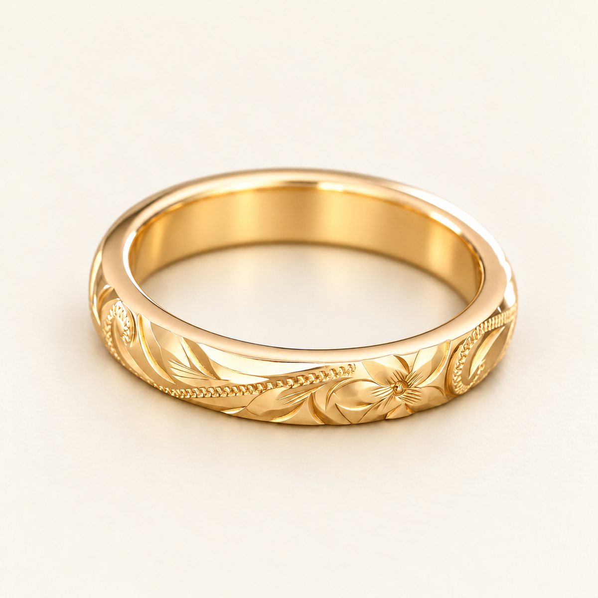Yellow gold Hawaiian ring with a heavy rounded 4mm profile and hand-engraved plumeria, leaves and scrollwork, shown on ivory.