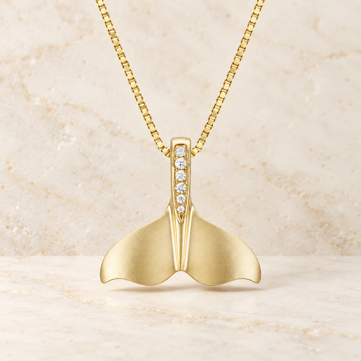 14K yellow gold diamond whale tail pendant against warm ivory stone