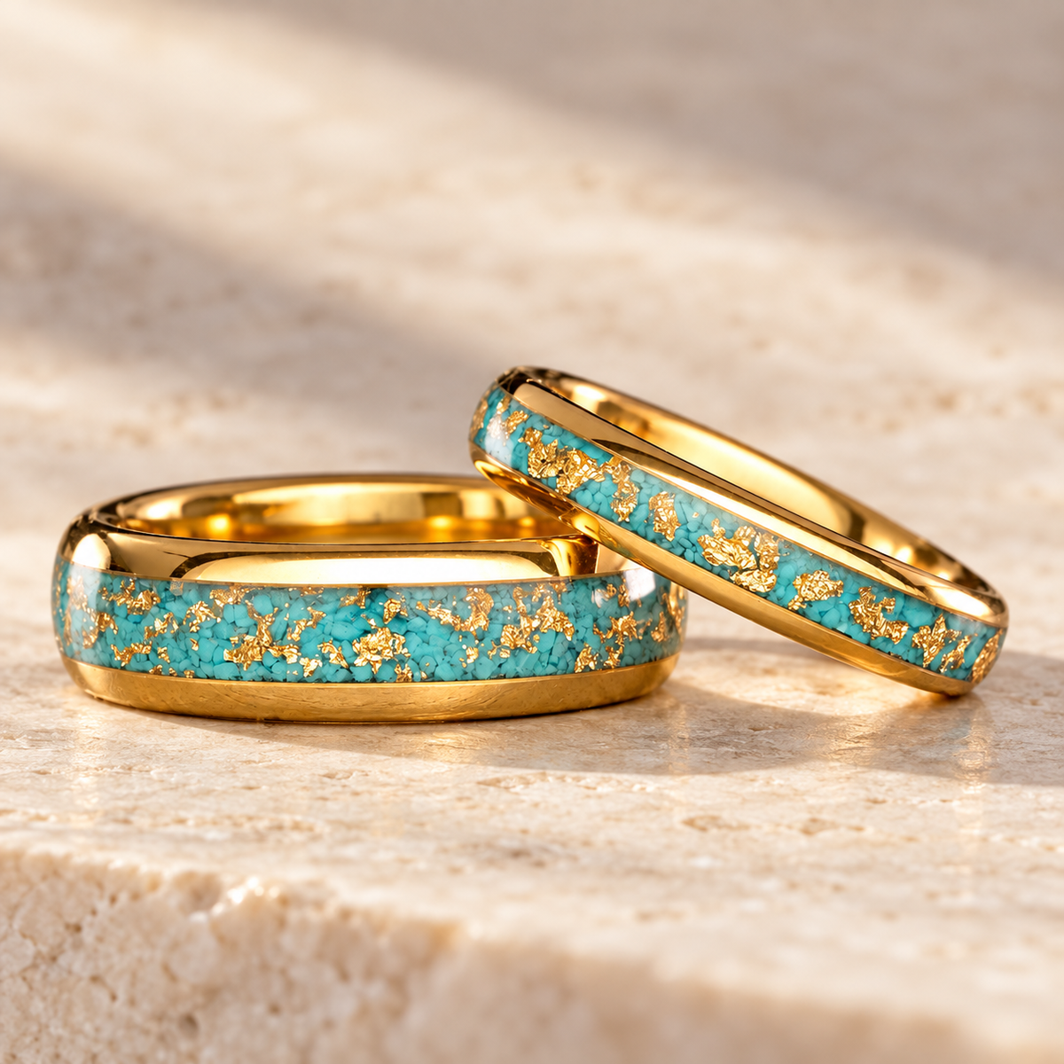 Turquoise and gold flake tungsten carbide ring pair on warm ivory stone