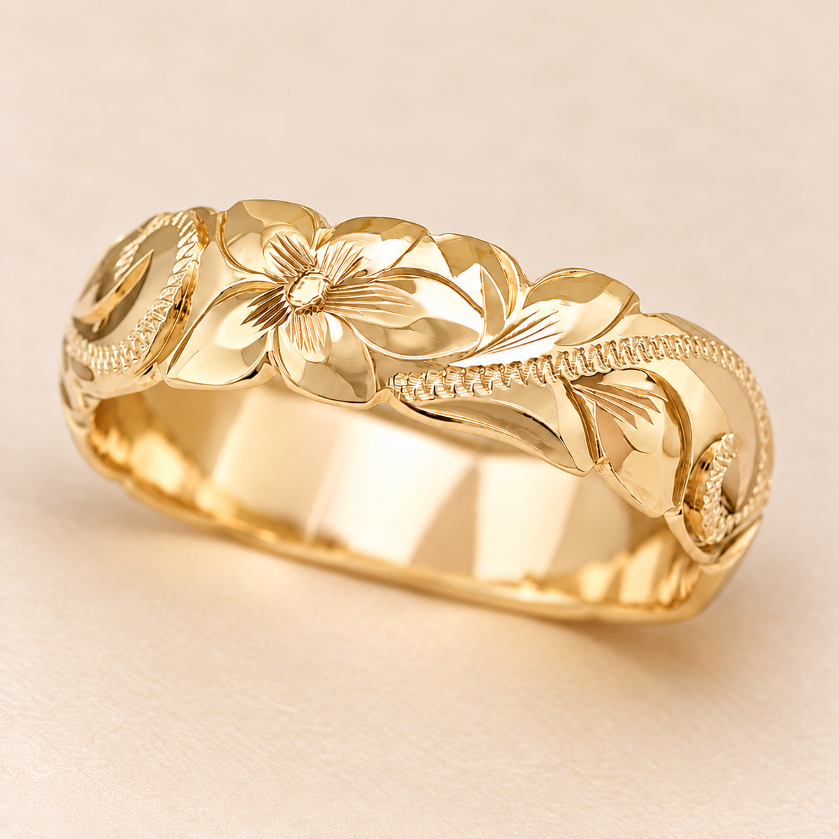 Close-up of a yellow gold 6mm Hawaiian ring with floral scroll engraving and scalloped wave edges on an ivory background.