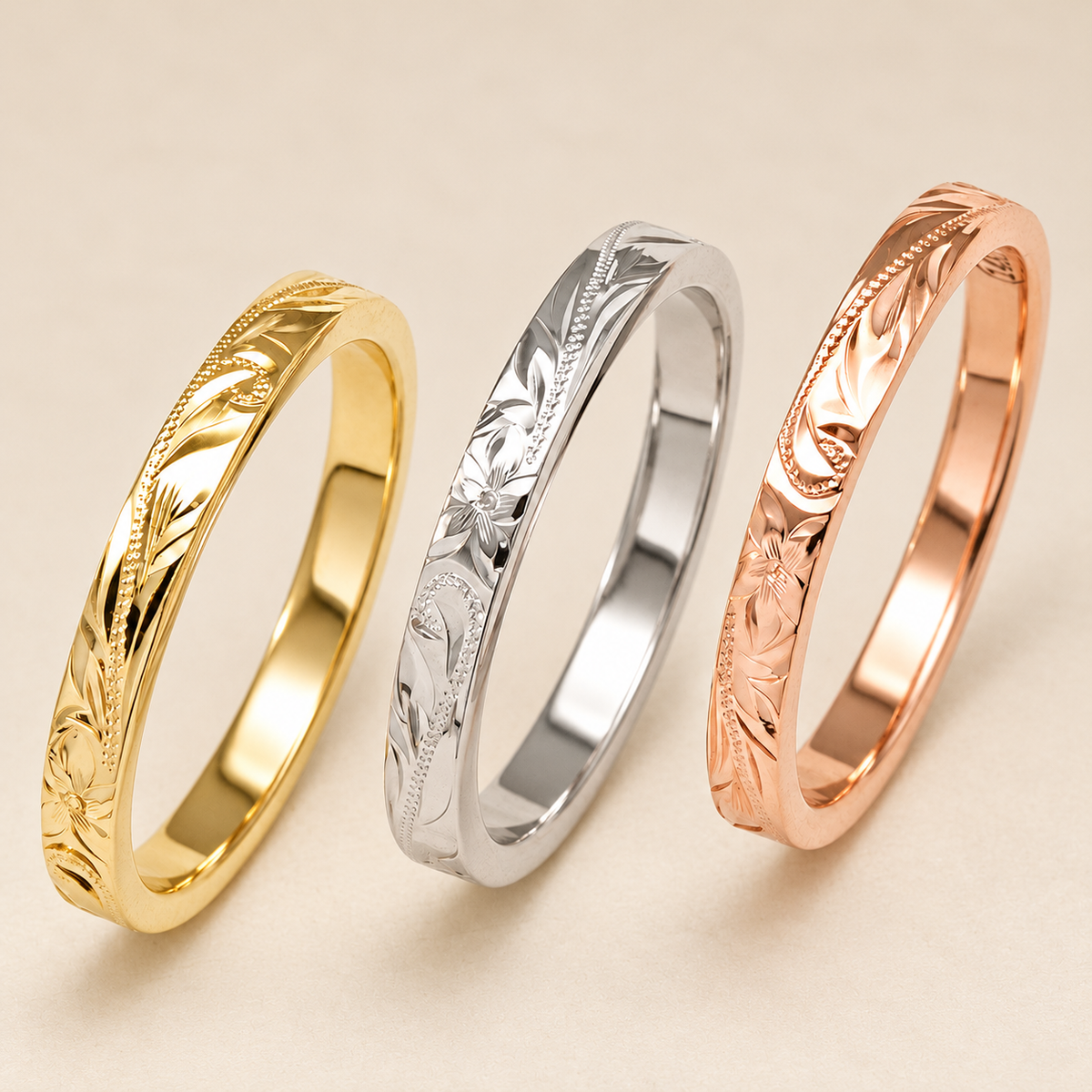 Three slim 2.5mm flat Hawaiian hand-engraved rings in yellow, white and rose gold on ivory.