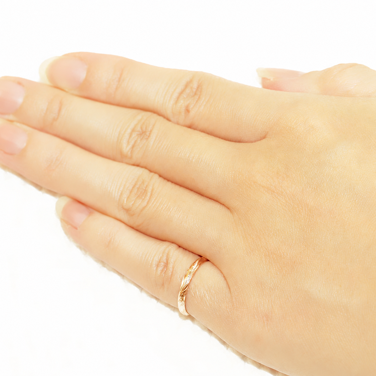 Hand wearing a slim 2mm 14K gold Hawaiian hand-engraved ring on a white background.