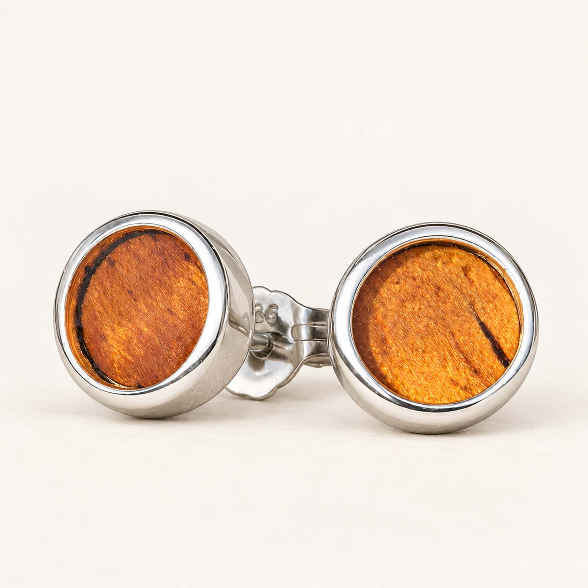 Pair of round 8mm koa wood sterling silver stud earrings with polished silver bezels and visible rear hardware, on a warm ivory background.