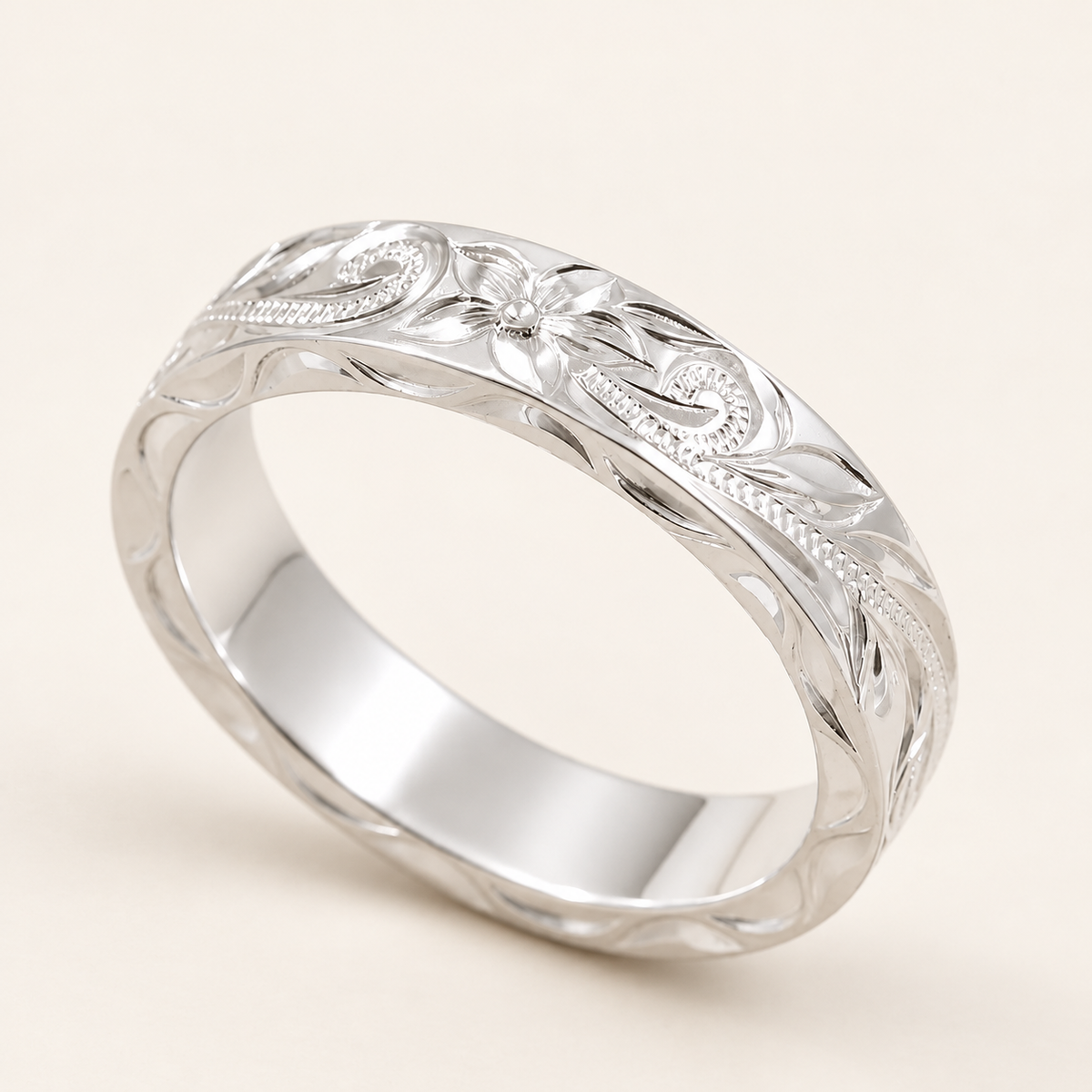 Sterling silver 4mm Hawaiian heritage ring with plumeria and scroll engraving, angled view on ivory