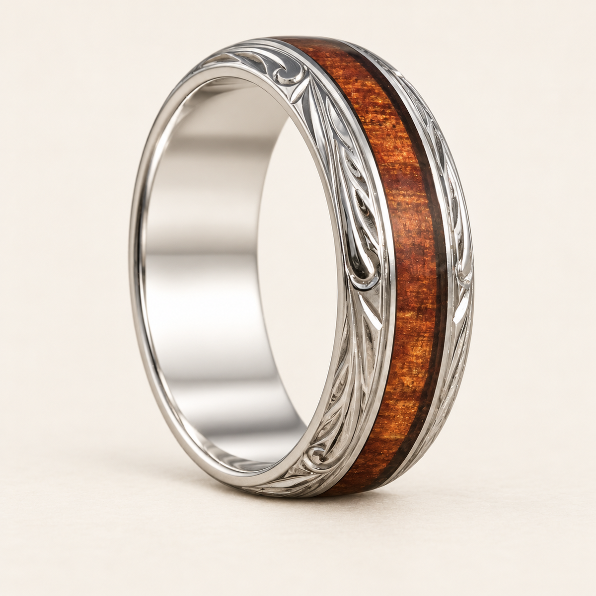 Upright sterling silver ring with a central Hawaiian koa wood inlay and hand-engraved leaf and scroll borders on an ivory background