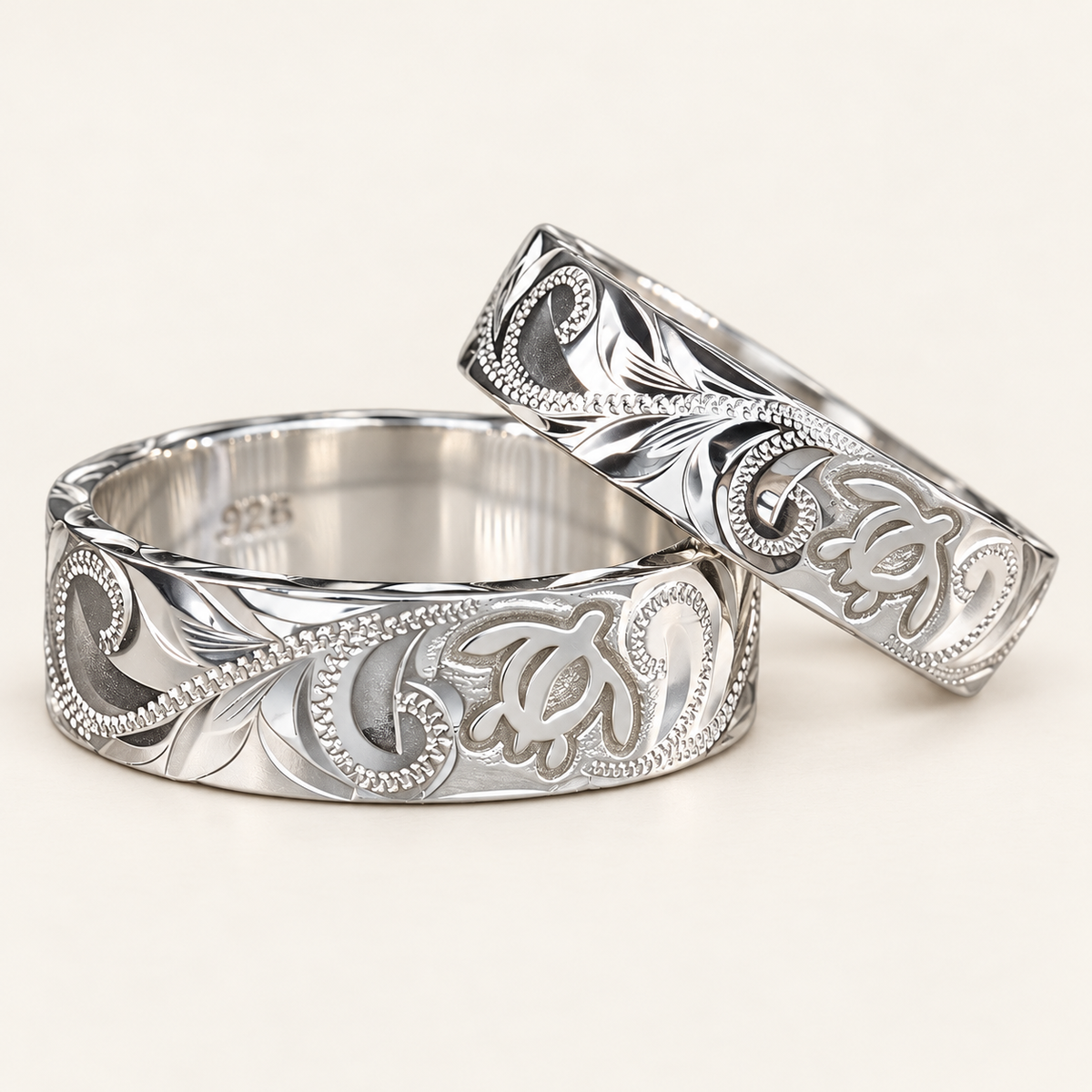 Angled pair of sterling silver Hawaiian honu rings with engraved turtle and scroll designs on an ivory background